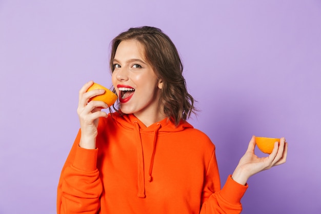 Immagine di una bella giovane donna eccitata che posa isolata sopra la parete viola della parete che tiene agrumi arancio.