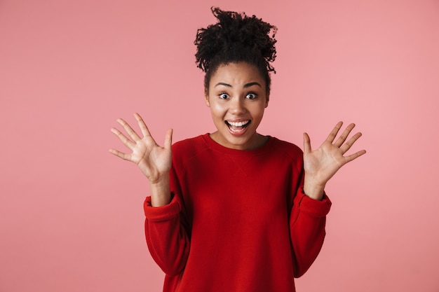 Immagine di una bellissima giovane donna africana eccitata felice che posa sopra la parete rosa.