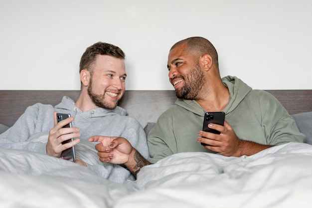 Immagine di una coppia gay felice, sui loro telefoni a letto