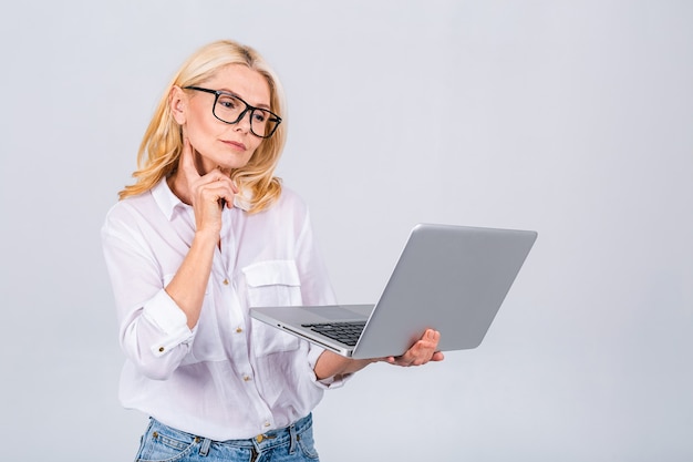 Immagine di una donna allegra di affari maturi in piedi isolato su sfondo bianco utilizzando il computer portatile. Ritratto di un computer portatile senior sorridente della tenuta della signora.