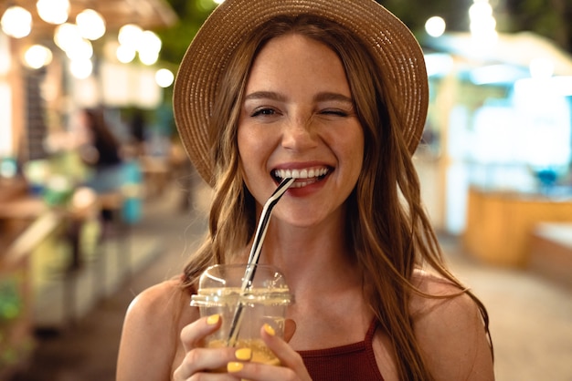 Immagine di una donna allegra felice ottimista positiva che cammina per strada all'aperto bevendo succo alla sera strizzando l'occhio.