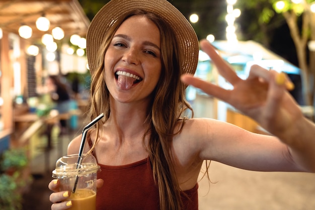 Immagine di una donna allegra felice ottimista positiva che cammina per strada all'aperto bevendo succo la sera sera mostrando pace.