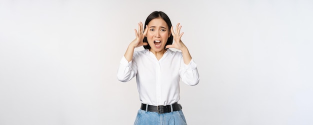 Immagine di una donna asiatica ansiosa scioccata in preda al panico che si tiene per mano sulla testa e si preoccupa in piedi frustrata e spaventata su sfondo bianco