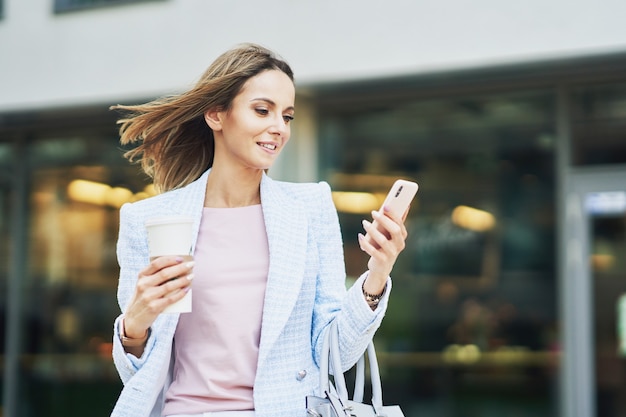 Immagine di una donna attraente adulta con uno smartphone che cammina in città