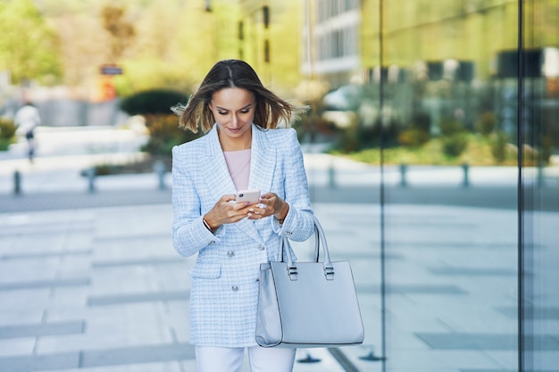 Immagine di una donna attraente adulta con uno smartphone che cammina in città