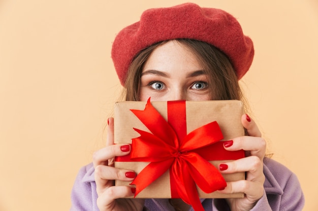 Immagine di una donna bruna 20s con i capelli lunghi sorridente e tenendo la confezione regalo, in piedi isolato