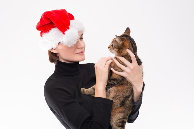 Immagine di una donna con un cappello di Babbo Natale che tiene in braccio un gatto. Sfondo chiaro dello studio. Tecnica mista