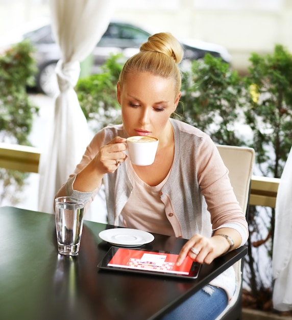 Immagine di una donna di mezza età che utilizza un tablet digitale mentre è seduta in un caffè all'aperto