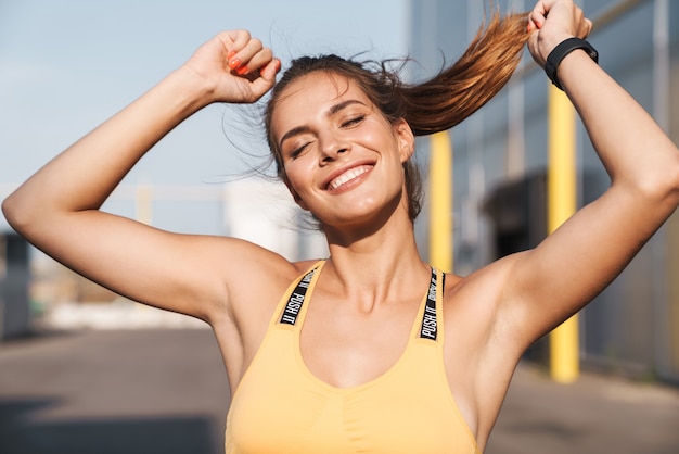 Immagine di una donna felice in abiti sportivi che sorride e cammina all'aperto in una mattina di sole