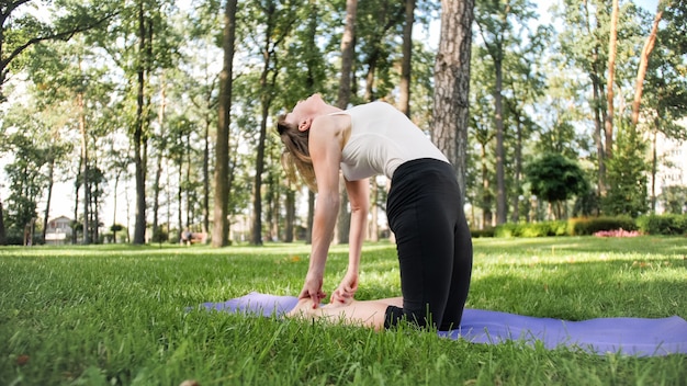 Immagine di una donna felice sorridente di mezza età che medita e fa esercizi di yoga sull'erba della foresta. Donna che si prende cura della sua salute fisica e mentale mentre pratica fitness e si estende al parco