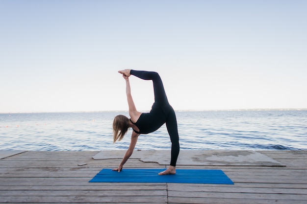 Immagine di una donna graziosa che fa yoga nel lago