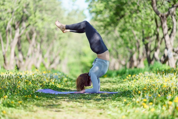 Immagine di una donna in piedi sulle mani che fa yoga nella foresta il giorno d'estate