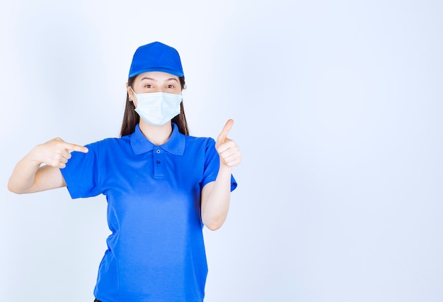 Immagine di una donna in uniforme che indossa una maschera medica che punta il pollice in su.