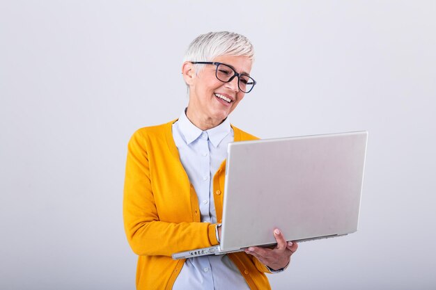 Immagine di una donna matura allegra in piedi isolata su uno sfondo grigio usando un computer portatile Ritratto di una signora anziana sorridente che tiene in mano un laptop