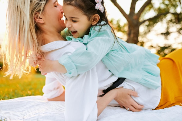 Immagine di una figlia felice che sorride e abbraccia sua madre trascorrendo del tempo insieme nel parco Giovane donna che gioca e si diverte con il suo bambino sull'erba verde Mamma e bambina condividono l'amore