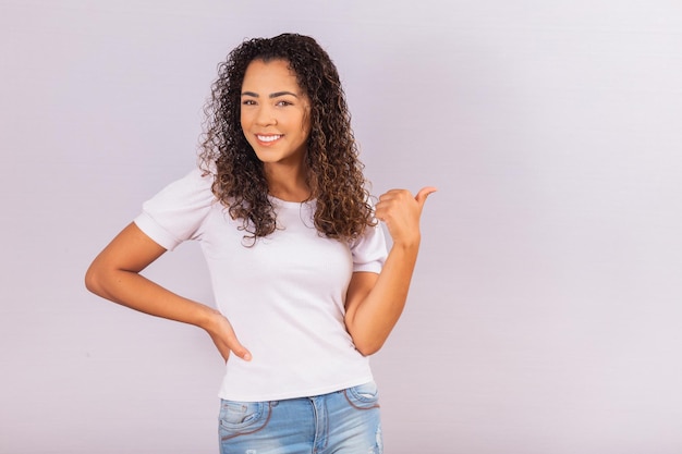 Immagine di una giovane donna afro allegra che indica con il pollice lo spazio libero per il testo.