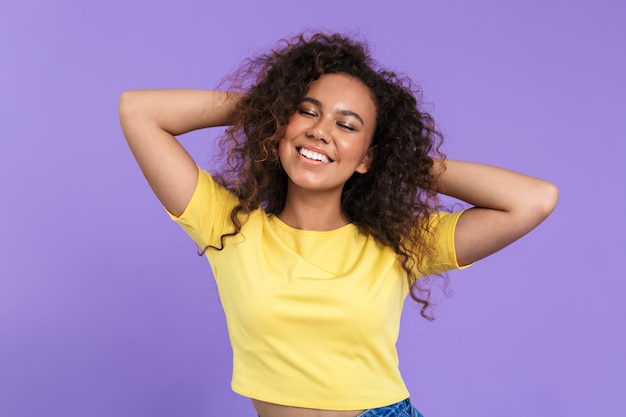 Immagine di una giovane donna afroamericana con i capelli ricci in posa con un sorriso isolato su un muro viola