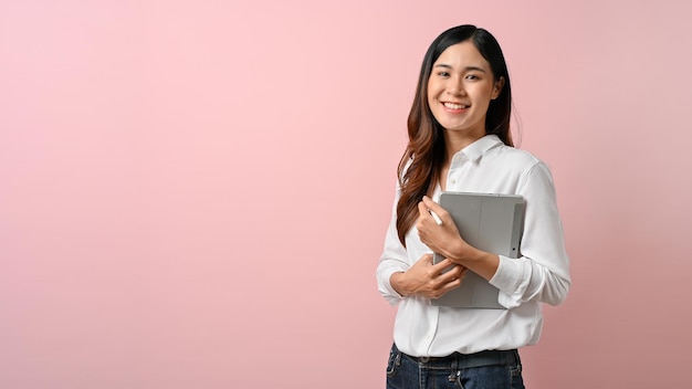 Immagine di una giovane donna asiatica che tiene il tablet in piedi con sfondo rosa isolato