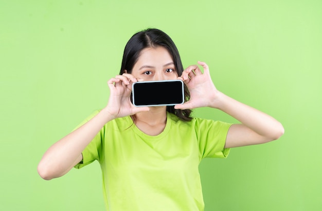 Immagine di una giovane donna asiatica che tiene in mano uno smartphone su sfondo verde