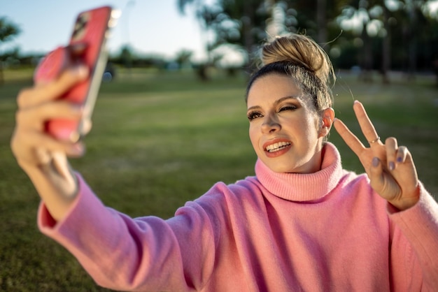 Immagine di una giovane donna bionda latina eccitata che fa felice selfie con il cellulare sullo sfondo del parco
