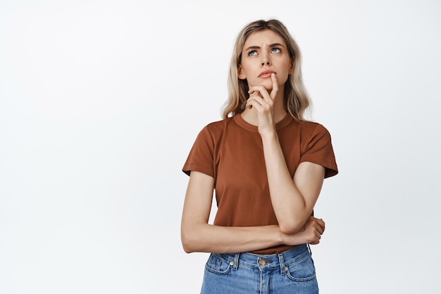 Immagine di una giovane donna che fa una scelta seria guardando in alto pensando a qualcosa in piedi su uno sfondo bianco
