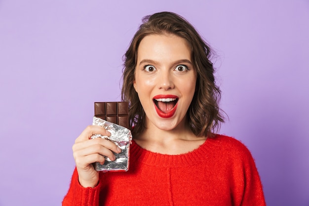Immagine di una giovane donna emotiva scioccata in posa isolata sul muro viola che tiene il cioccolato.