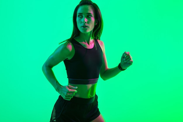 Immagine di una giovane donna sportiva seria e forte isolata sul muro blu con luci al neon in esecuzione.