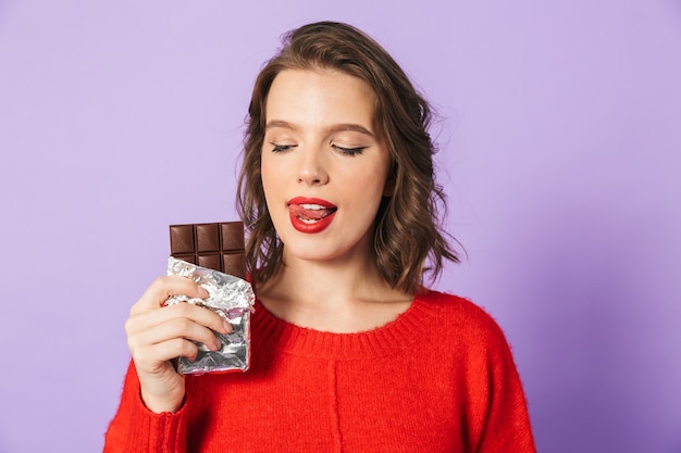 Immagine di una giovane e bella donna in posa isolata sopra la parete viola della holding del muro di cioccolato.