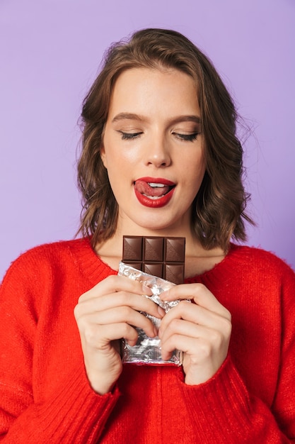 Immagine di una giovane e bella donna in posa isolata sopra la parete viola della holding del muro di cioccolato.