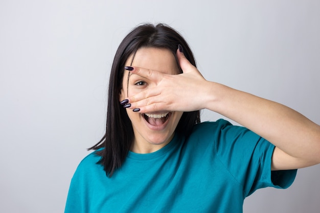 Immagine di una ragazza adolescente bruna che copre il viso con le mani e fa capolino tra le dita.