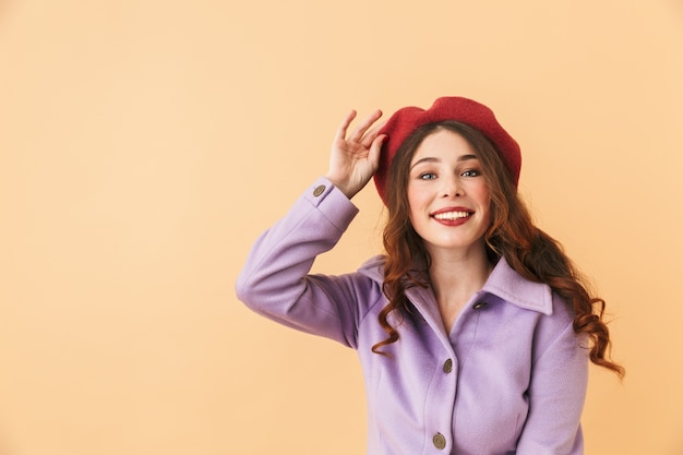 Immagine di una ragazza affascinante 20s in cappotto e cappello che ride, mentre in piedi isolato