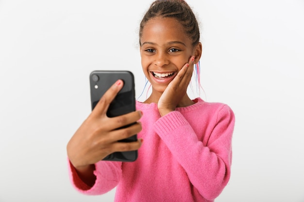 Immagine di una ragazza afroamericana eccitata che fa una videochiamata sul cellulare isolato su un muro bianco