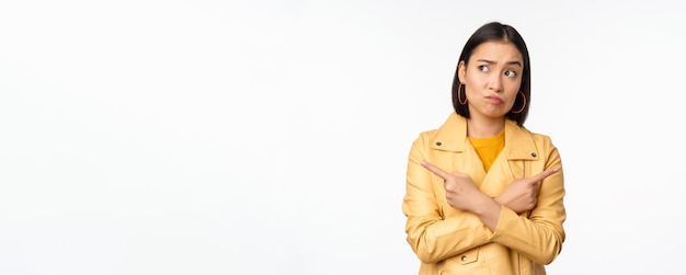 Immagine di una ragazza asiatica indecisa che punta le dita lateralmente verso sinistra e destra scegliendo la variante de