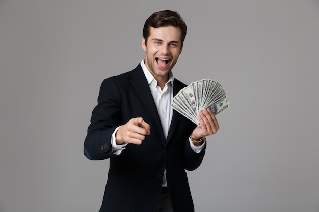 Immagine di uomo d'affari anni '30 in tuta sorridente e in possesso di fan di soldi in banconote in dollari, isolato sopra il muro grigio