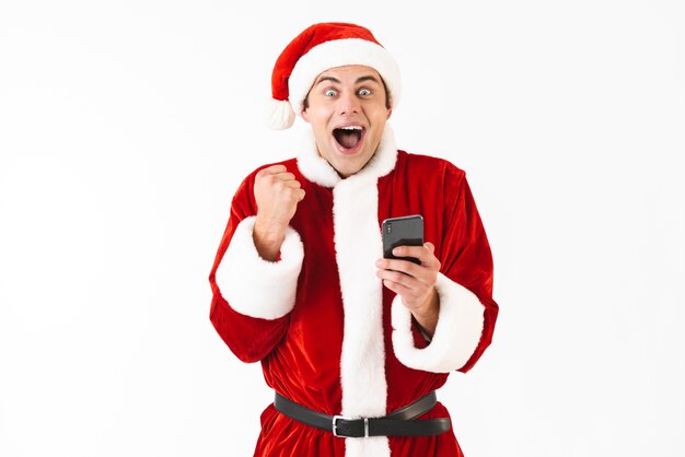 Immagine di uomo eccitato 30 anni in costume di Babbo Natale tenendo il telefono cellulare