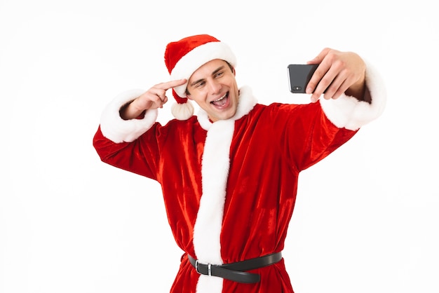 Immagine di uomo ottimista anni '30 in costume di Babbo Natale tenendo lo smartphone e prendendo selfie