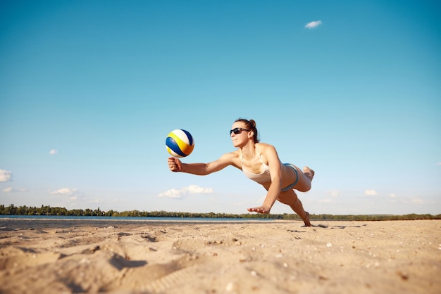 Immagine dinamica di una giovane donna in movimento che gioca a beach volley colpendo la palla e cadendo sopra