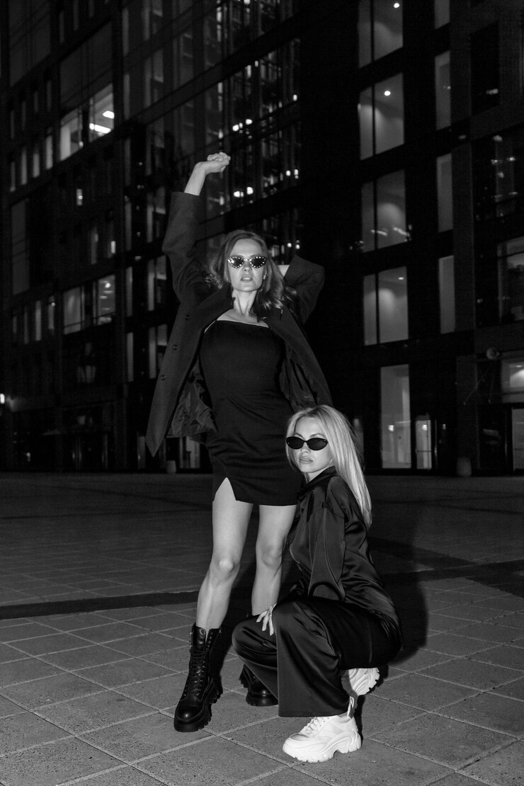 Immagine in bianco e nero di due donne lesbiche positive che posano di notte sullo sfondo delle luci della città Giovani femmine alla moda che guardano la fotocamera nella strada notturna