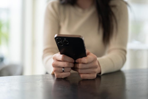 Immagine in primo piano di una donna asiatica seduta a un tavolo e che usa il suo smartphone