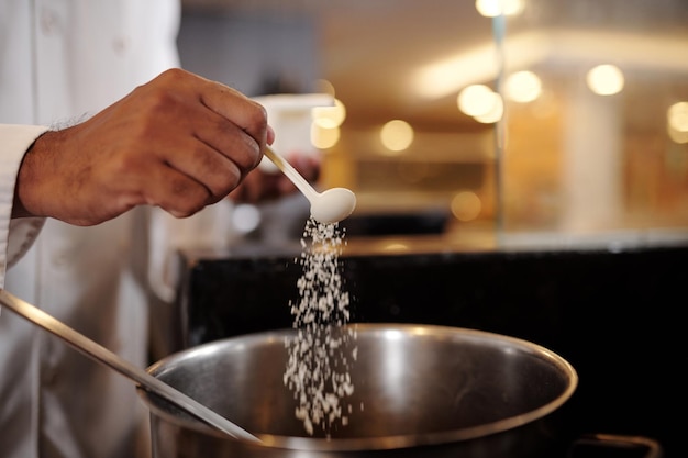 Immagine in primo piano di uno chef che mette un cucchiaio di sale in una grande pentola