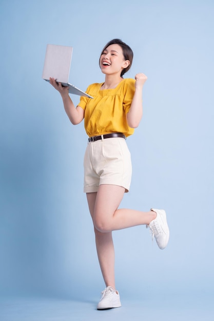 Immagine integrale della giovane ragazza asiatica che per mezzo del computer portatile su fondo blu