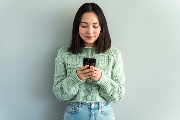 Immagine interna di adorabile donna caucasica isolata su sfondo grigio sorridente felicemente e divertita dal contenuto sullo schermo dello smartphone che tiene con entrambe le mani