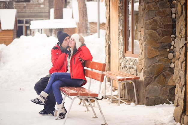 Immagine luminosa della coppia di famiglia in abiti invernali seduto su una panca in legno