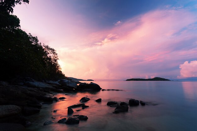 Immagine lunga di esposizione del cielo drammatico e del paesaggio marino dell&#39;onda con roccia nel tramonto