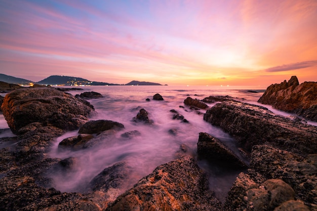 Immagine lunga esposizione di vista sul mare drammatico del cielo con la roccia nella priorità bassa di paesaggio del tramonto