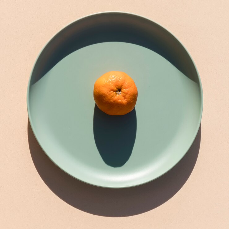 Immagine minimalista di un mandarino su un piatto verde chiaro con uno sfondo beige