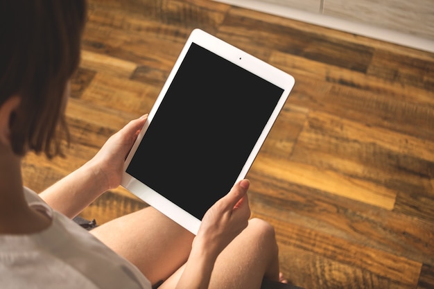 Immagine mockup con ragazza in appartamento e tablet pc in mano, foto di sfondo in legno con spazio copia
