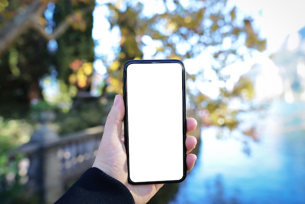 Immagine mockup della mano che tiene il telefono cellulare con schermo vuoto con sfondo verde e la natura del lago