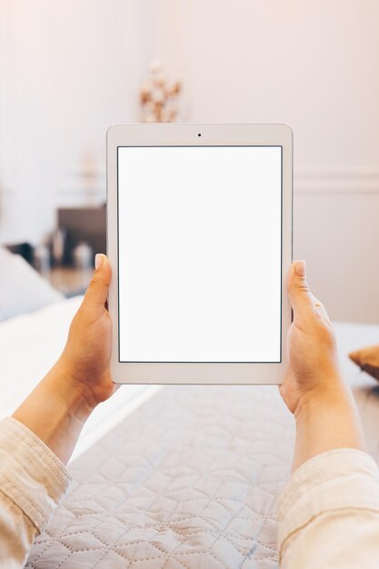 Immagine mockup della mano della donna che tiene tablet pc bianco con schermo bianco vuoto a casa