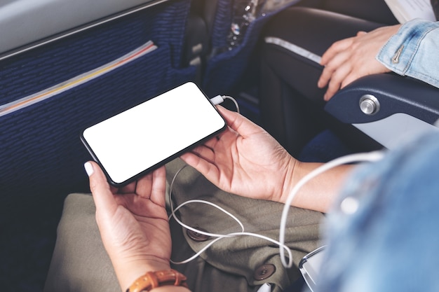 Immagine mockup della mano di una donna che tiene uno smartphone nero con schermo desktop vuoto e auricolare in cabina